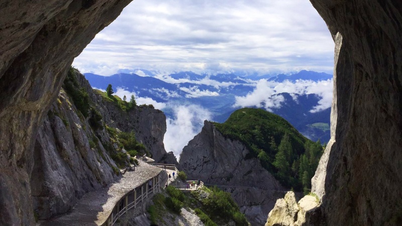 Grottmynning med utsikt over alperna med vita moln pa resan t Abtenau